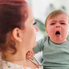 Płacz dziecka, być może z powodu objawów RSV, w ramionach mamy.