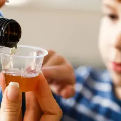 Dziecko patrzy, jak dorosły nalewa syrop z butelki do miarki.