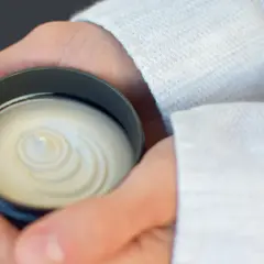 Dłonie trzymające słoiczek z białą, kremową maścią o spiralnym wzorze.