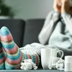 Stopy w kolorowych skarpetach, osoba owinięta kocem z chusteczkami i lekami.