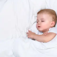 Słodki sen niemowlaka, nawet jeśli czasem towarzyszy mu ciche chrapanie. Maluch odpoczywa otulony białym kocykiem.