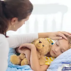 Matka czule głaszcze śpiące dziecko z misiem. Zastanawia się, ile trwa kaszel u dziecka i czy potrzebna jest kolejna wizyta u lekarza.