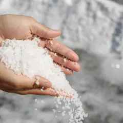Dłonie trzymające kryształki soli emskiej, która przesypuje się między palcami.