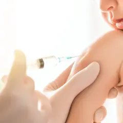 Małe dziecko otrzymuje szczepionkę 6w1. Ręka w rękawiczce trzyma strzykawkę, podając zastrzyk w ramię malucha.