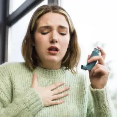 Kobieta z astmą używa inhalatora, trzymając rękę na klatce piersiowej.