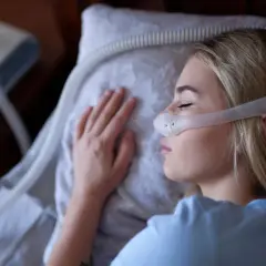 Kobieta śpi z maską CPAP na twarzy, obok stoi aparat do terapii bezdechu sennego.