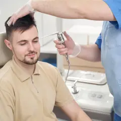 Lekarz w rękawiczkach bada ucho pacjenta otoskopem.