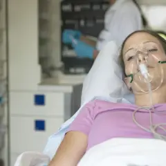 Kobieta w masce tlenowej leżąca w łóżku szpitalnym.