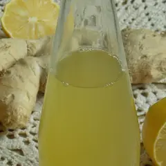 Szklana butelka z żółtym syropem, obok korzenie imbiru i połówki cytryny.