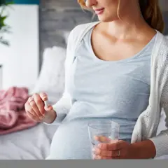 Ciężarna kobieta trzyma kapsułkę i szklankę wody.