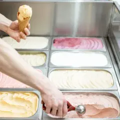 Ręce nakładają lody do wafelka i z pojemnika w lodziarni.