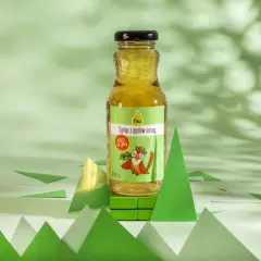 Butelka syropu z pędów sosny na zielonym tle, otoczona papierowymi choinkami.