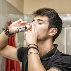 Mężczyzna aplikuje krople do nosa z buteleczki.