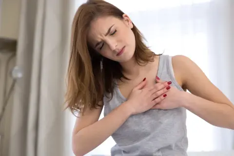 Kobieta trzymająca się za klatkę piersiową z wyrazem bólu na twarzy.