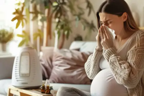 Ciężarna kobieta z chusteczką w dłoniach, siedząca na kanapie obok nawilżacza powietrza.