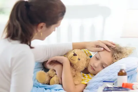 Matka czule głaszcze śpiące dziecko z misiem. Zastanawia się, ile trwa kaszel u dziecka i czy potrzebna jest kolejna wizyta u lekarza.