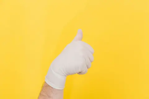 Ręka w białej rękawiczce pokazuje kciuk w górę. To gest aprobaty, mimo że uczulenie na lateks może być problemem.