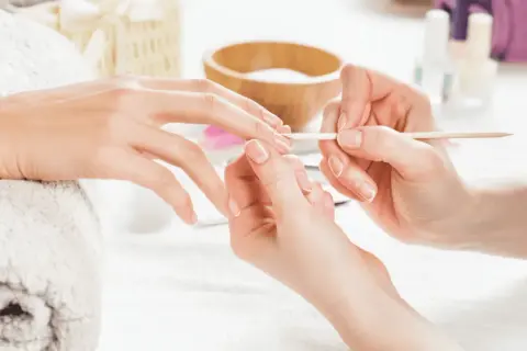 Dłoń przygotowywana do manicure hybrydowego. Delikatne ruchy patyczkiem usuwają skórki, by uniknąć uczulenia na hybrydę.