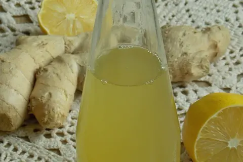 Szklana butelka z żółtym syropem, obok korzenie imbiru i połówki cytryny.