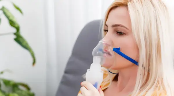 Kobieta z maską nebulizatora na twarzy.
