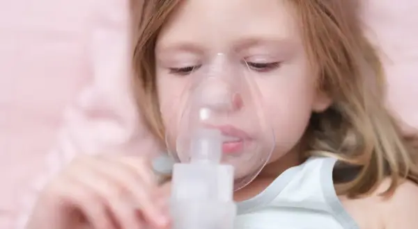 Dziewczynka z maską inhalatora na twarzy.