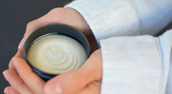 Dłonie trzymające słoiczek z białą, kremową maścią o spiralnym wzorze.