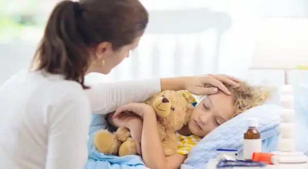 Matka czule głaszcze śpiące dziecko z misiem. Zastanawia się, ile trwa kaszel u dziecka i czy potrzebna jest kolejna wizyta u lekarza.