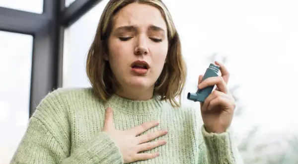 Kobieta z astmą używa inhalatora, trzymając rękę na klatce piersiowej.