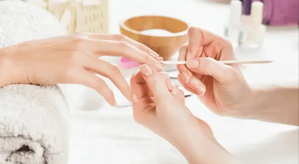 Dłoń przygotowywana do manicure hybrydowego. Delikatne ruchy patyczkiem usuwają skórki, by uniknąć uczulenia na hybrydę.