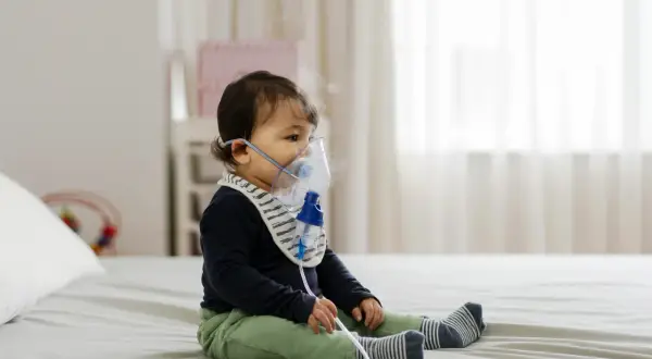 Małe dziecko w maseczce inhalacyjnej. Delikatna para unosząca się z nebulizatora świadczy o tym, że odbywają się inhalacje dla niemowlaka.