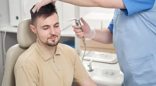Lekarz w rękawiczkach bada ucho pacjenta otoskopem.