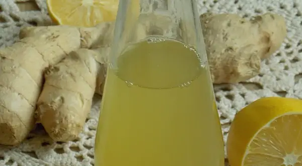 Szklana butelka z żółtym syropem, obok korzenie imbiru i połówki cytryny.