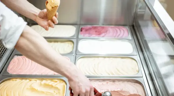 Ręce nakładają lody do wafelka i z pojemnika w lodziarni.