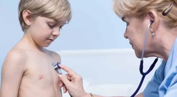 Lekarz osłuchuje klatkę piersiową chłopca, diagnozując zapalenie oskrzeli u dzieci.