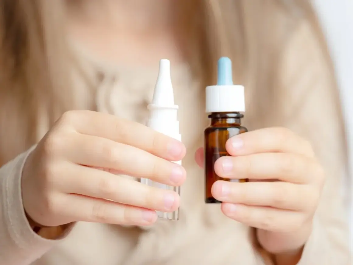 Dziecko trzyma w dłoniach dwa opakowania z kroplami do nosa: biały spray i brązową buteleczkę z pipetą.