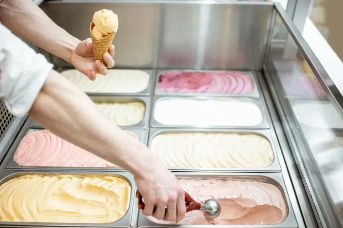 Ręce nakładają lody do wafelka i z pojemnika w lodziarni.