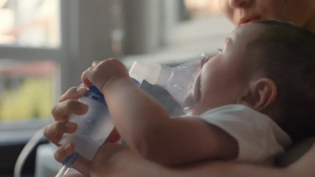 Mama pomaga niemowlęciu z suchym kaszlem, podając mu inhalator.
