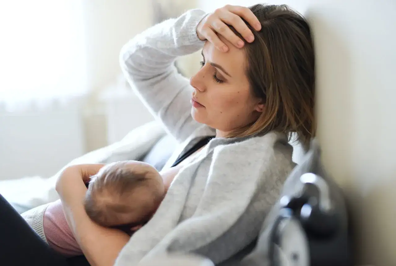 Zmęczona mama karmi piersią, zastanawia się, czy ibuprofen przy karmieniu piersią jest bezpieczny.