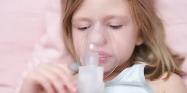 Dziewczynka z maską inhalatora na twarzy.