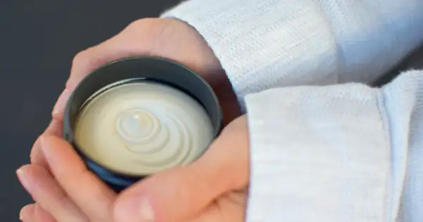 Dłonie trzymające słoiczek z białą, kremową maścią o spiralnym wzorze.