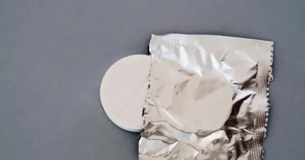 Biała tabletka z nacięciem obok srebrnego opakowania na szarym tle.