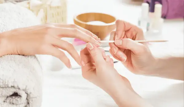 Dłoń przygotowywana do manicure hybrydowego. Delikatne ruchy patyczkiem usuwają skórki, by uniknąć uczulenia na hybrydę.