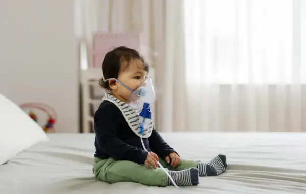 Małe dziecko w maseczce inhalacyjnej. Delikatna para unosząca się z nebulizatora świadczy o tym, że odbywają się inhalacje dla niemowlaka.
