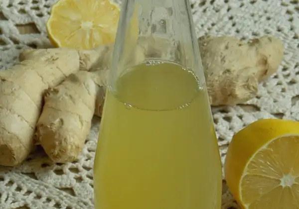 Szklana butelka z żółtym syropem, obok korzenie imbiru i połówki cytryny.